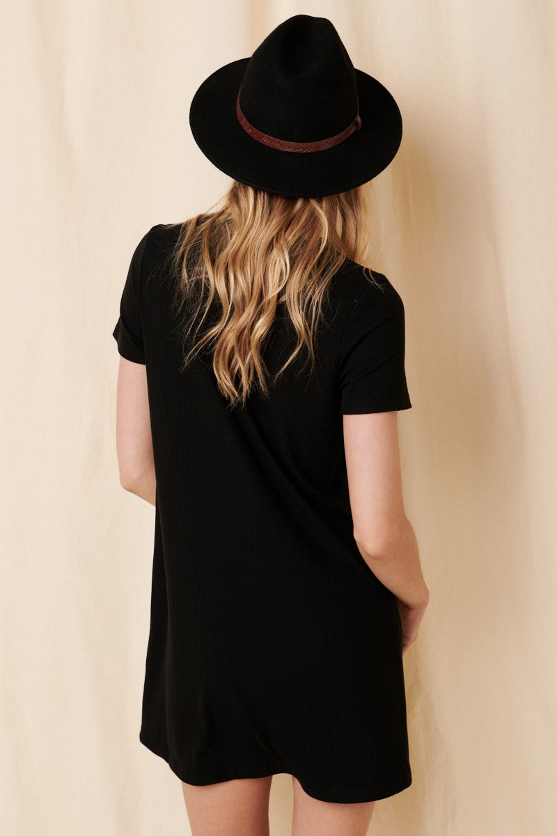 woman wearing a black short sleeve dress and a black hat, viewed from the back against a neutral background
