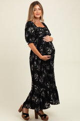woman wearing a black floral maternity maxi dress and holding her baby bump