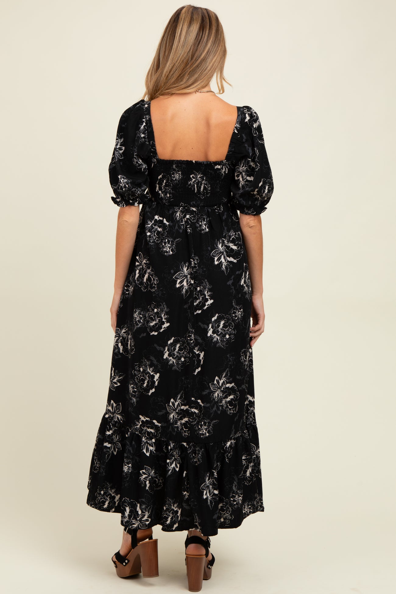 woman wearing a black floral maternity maxi dress with short puff sleeves and a ruffled hem, showing her baby bump