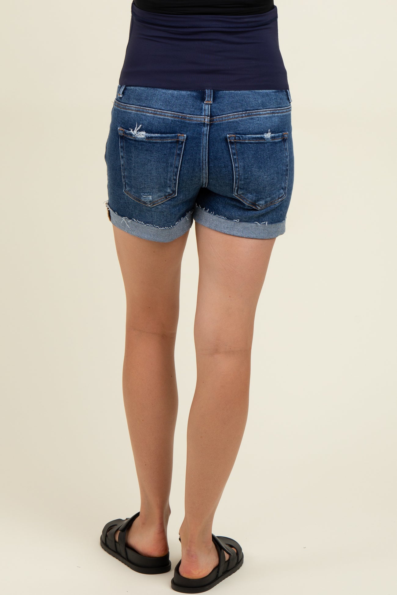 woman wearing dark denim maternity shorts with a stretchy waistband and frayed hem, showing a casual style.