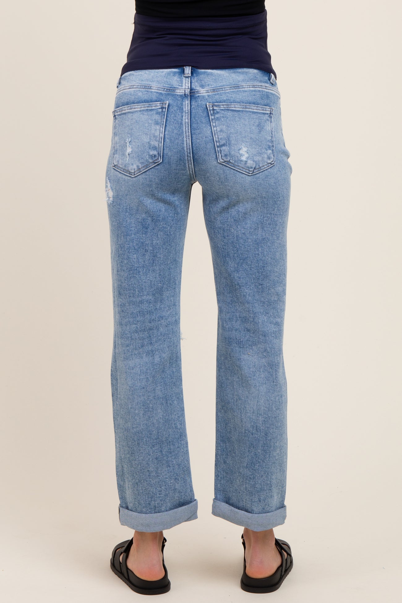 woman wearing light blue distressed maternity jeans with rolled cuffs, showing the back view