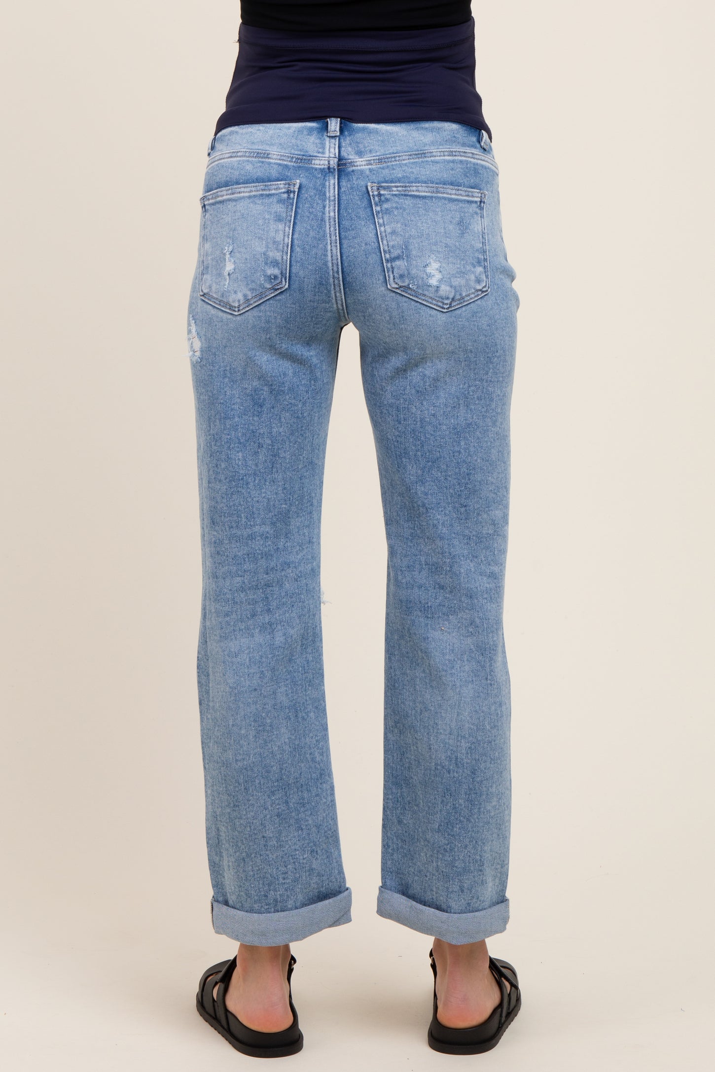 woman wearing light blue distressed maternity jeans with rolled cuffs, showing the back view