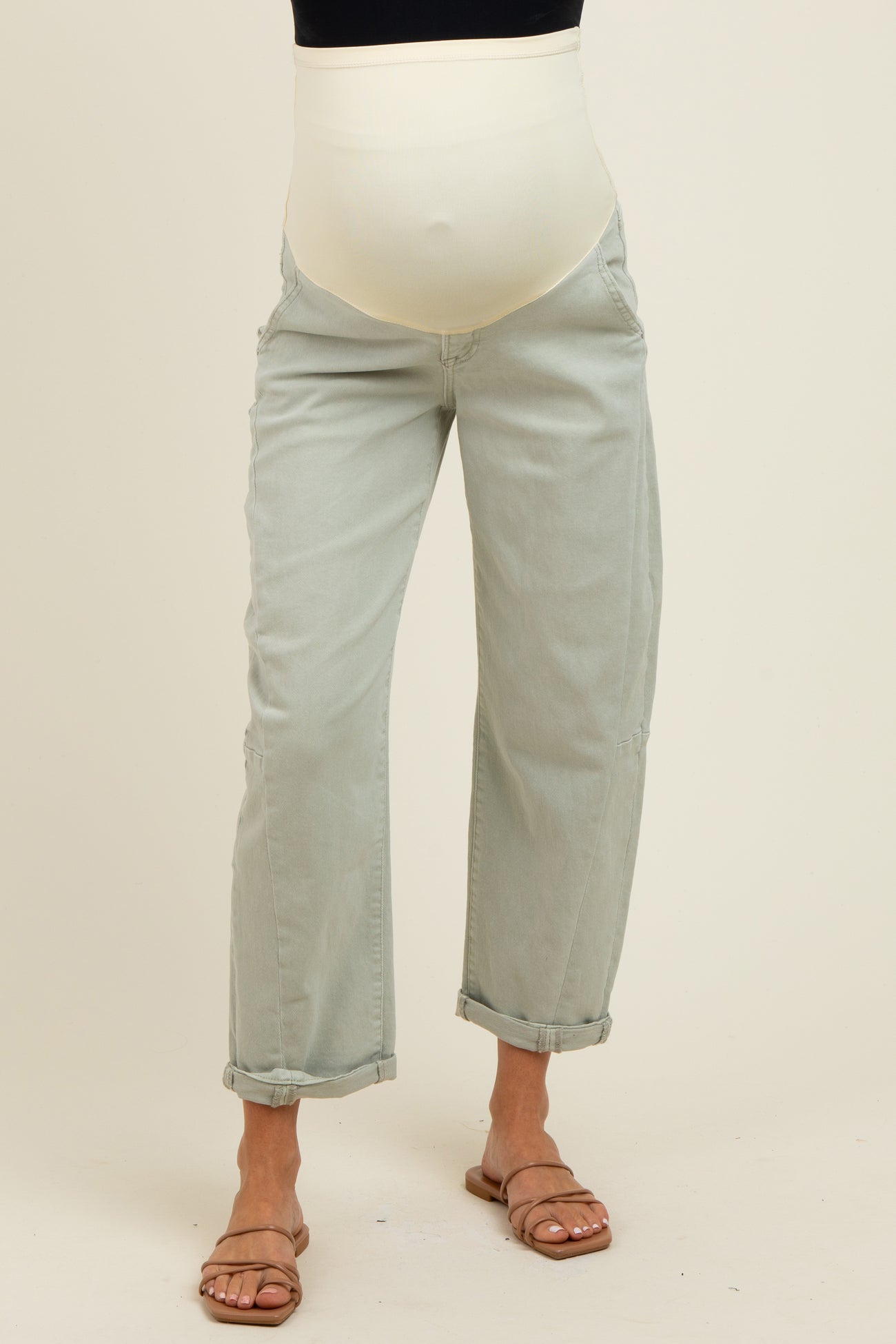 woman wearing light green maternity jeans with a white over-the-bump waistband and rolled-up cuffs, showcasing her baby bump