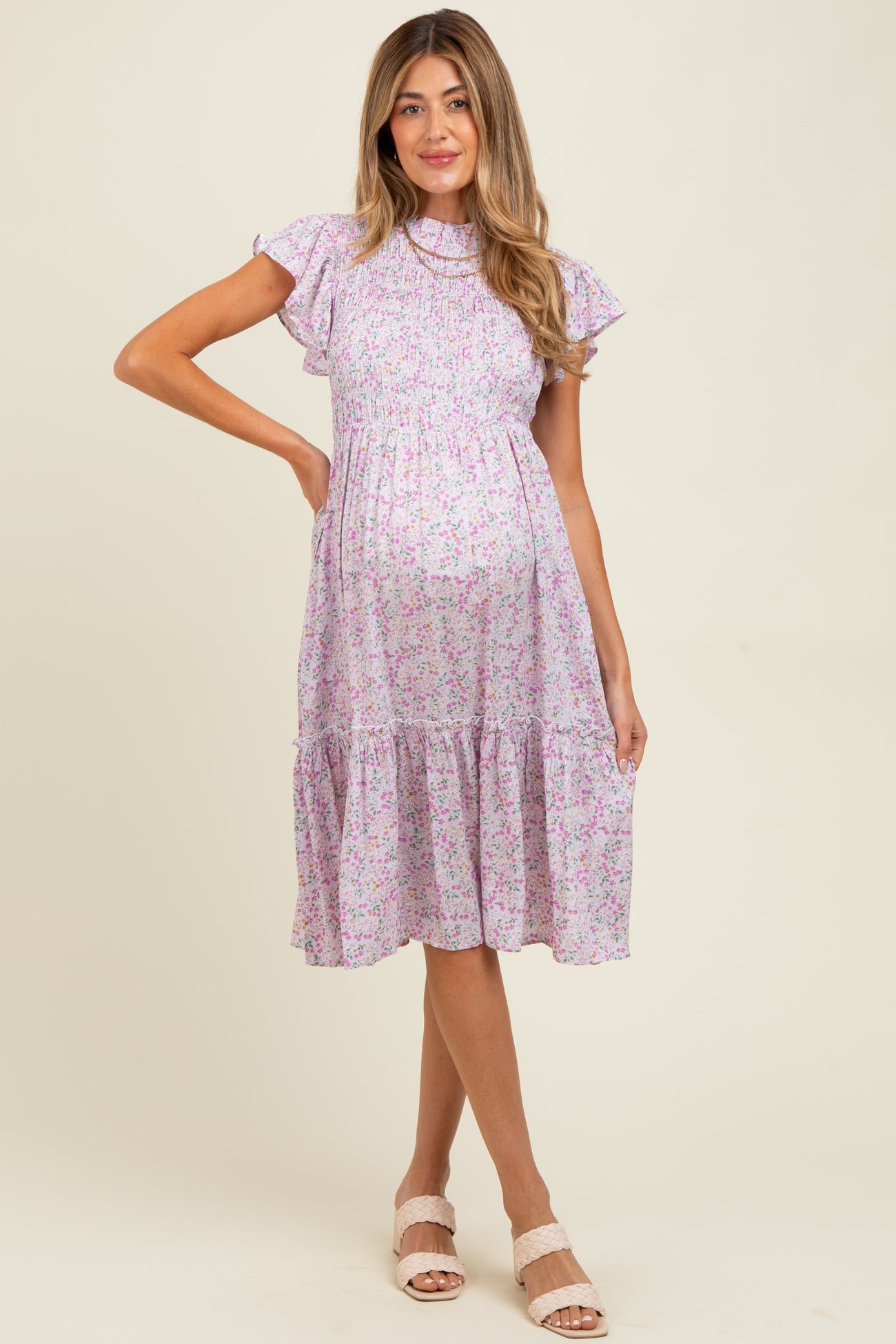 woman wearing a lilac floral maternity dress with ruffle sleeves and a tiered skirt, showing her baby bump