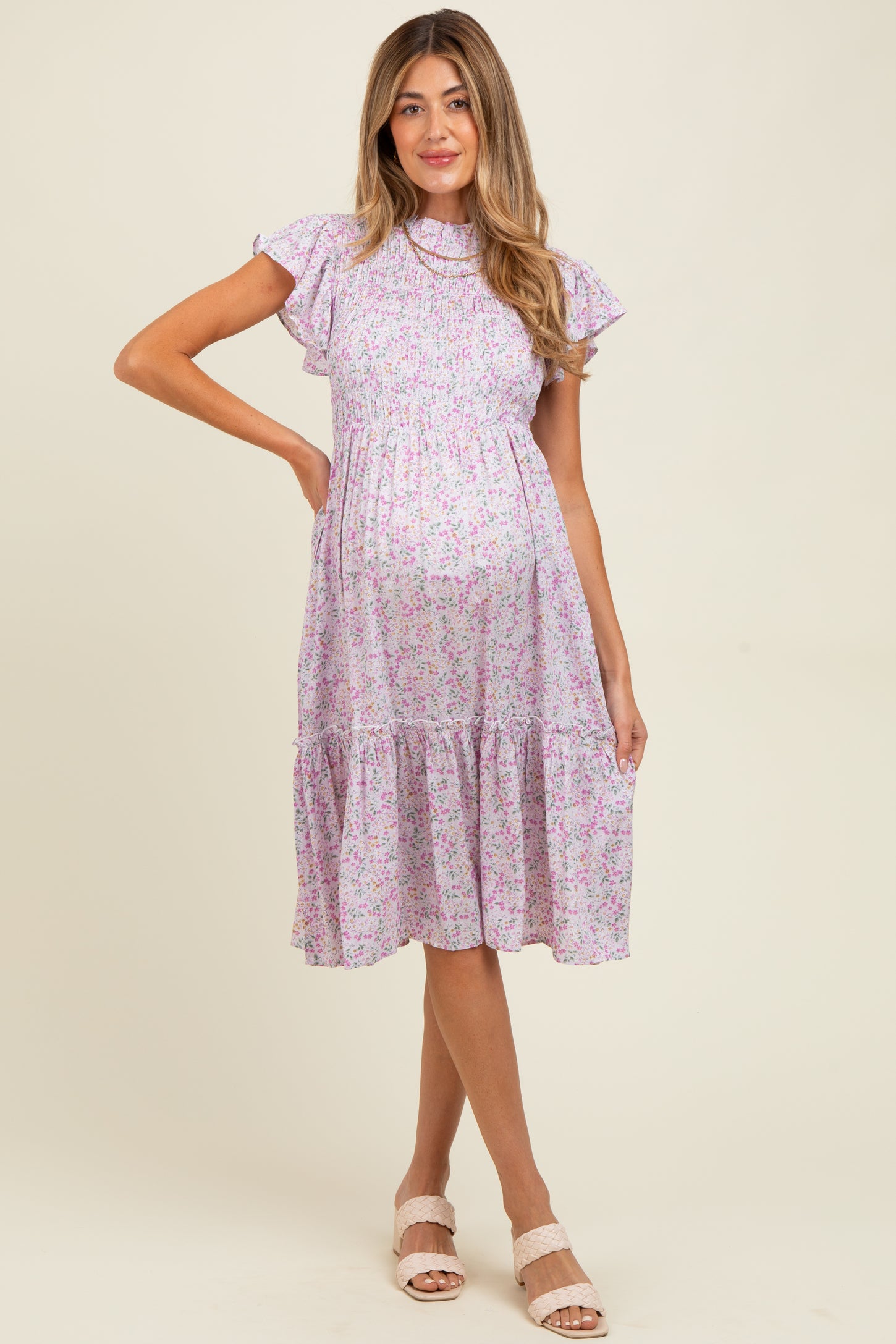 woman wearing a lilac floral maternity dress with ruffle sleeves and a tiered skirt, showing her baby bump