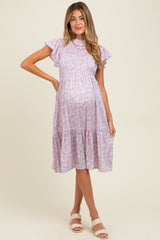 woman wearing a lilac floral maternity dress with ruffle sleeves and a tiered skirt, showing her baby bump