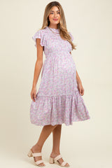 woman wearing a lilac floral maternity dress with short ruffled sleeves and a tiered skirt, showing her baby bump