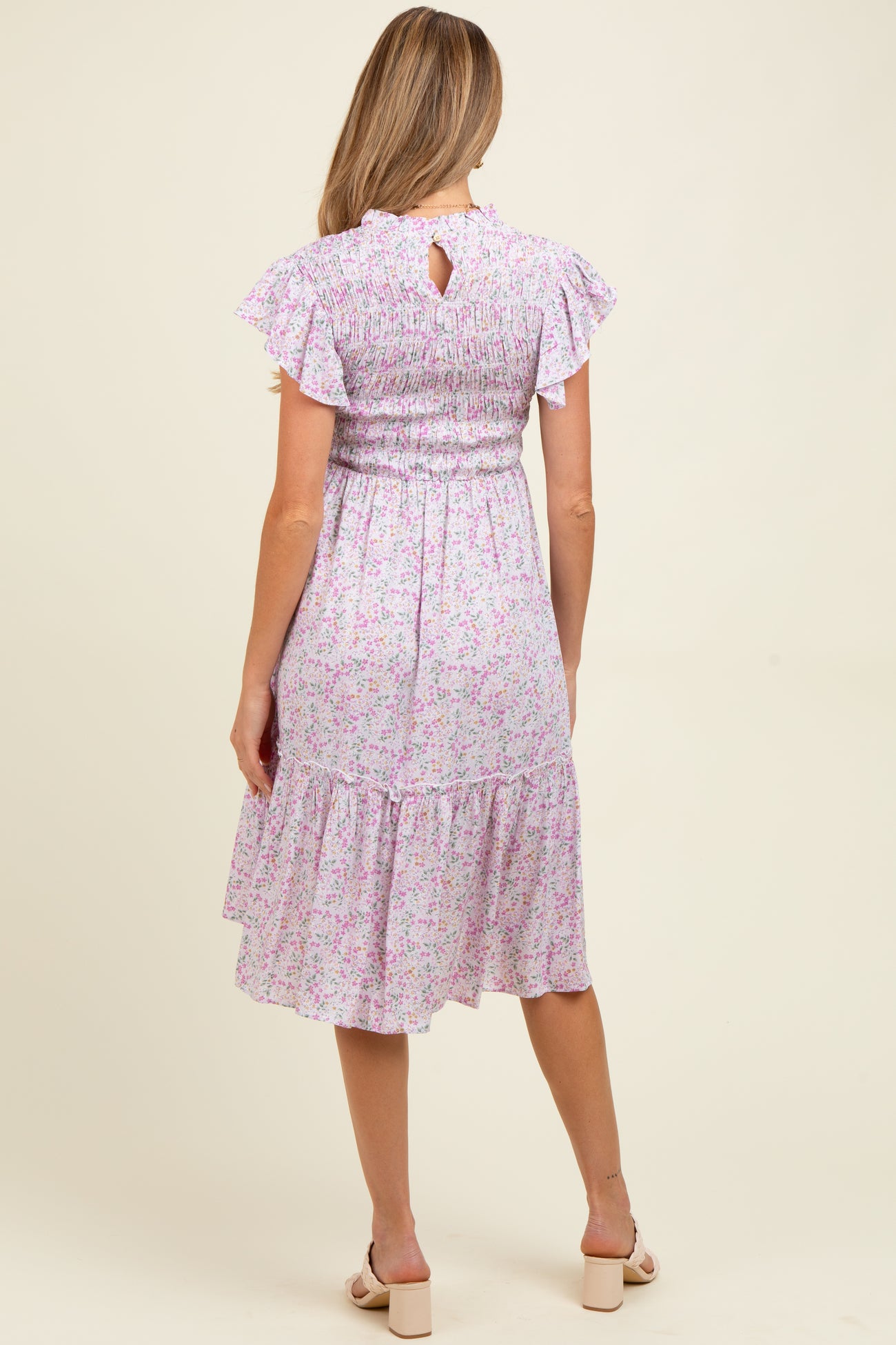 woman wearing a floral print maternity dress with ruffled sleeves and a smocked bodice, showing a baby bump from the back