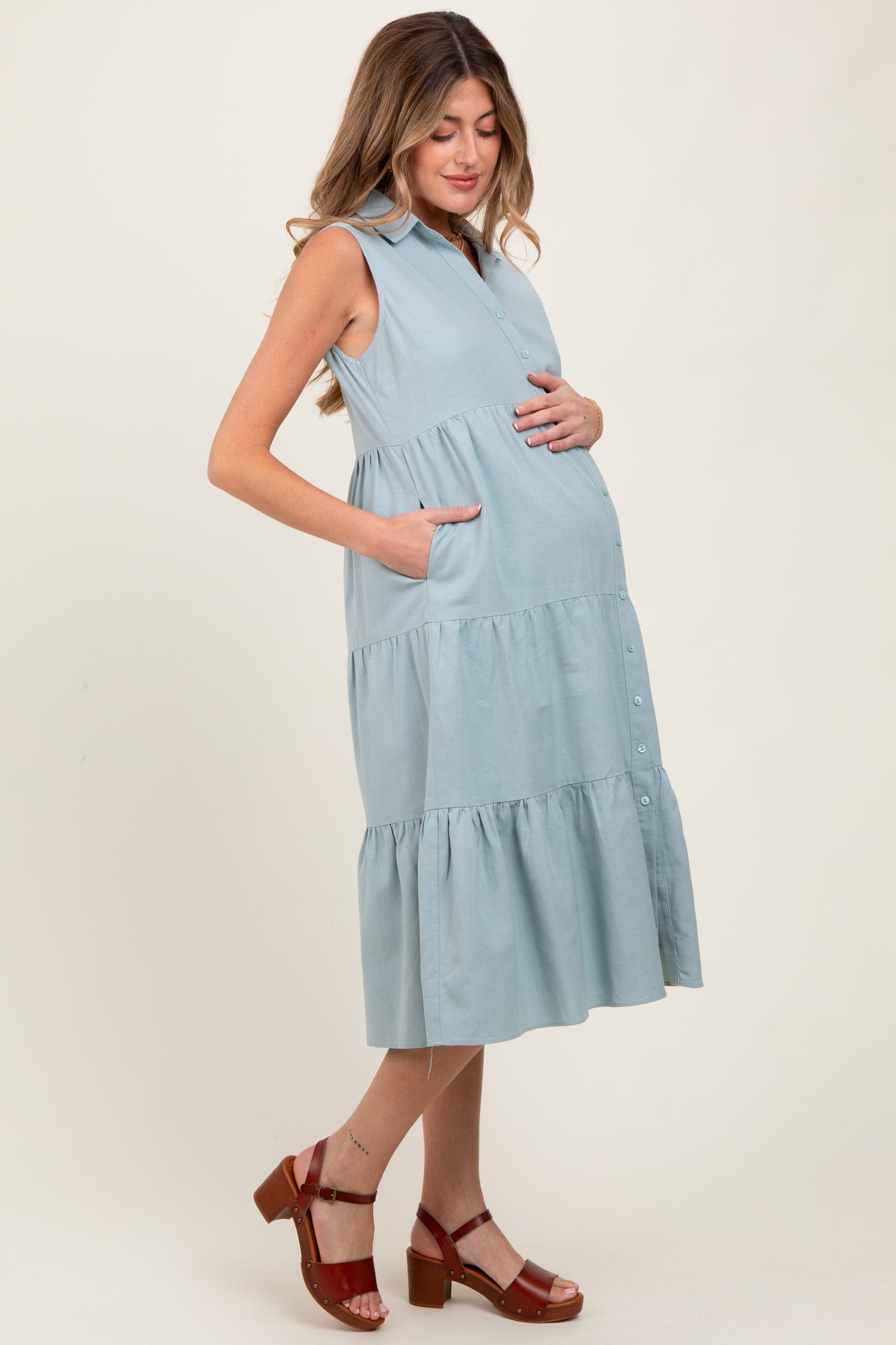 woman wearing a light blue sleeveless maternity dress with pockets and tiered skirt, showing baby bump