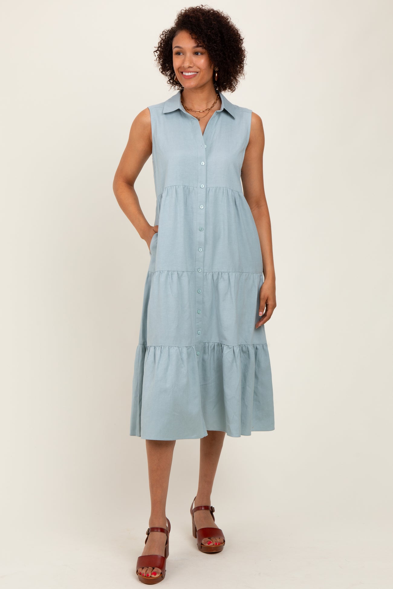 woman wearing a light blue sleeveless button-up midi dress with tiered layers and side pockets