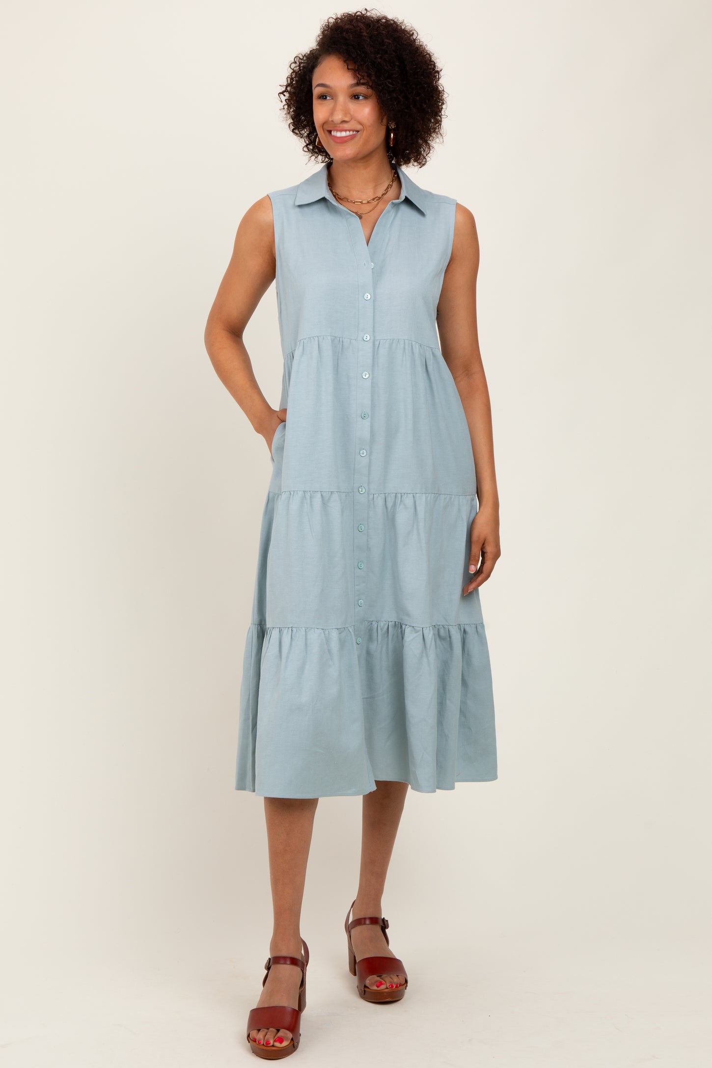 woman wearing a light blue sleeveless button-up midi dress with tiered layers and side pockets