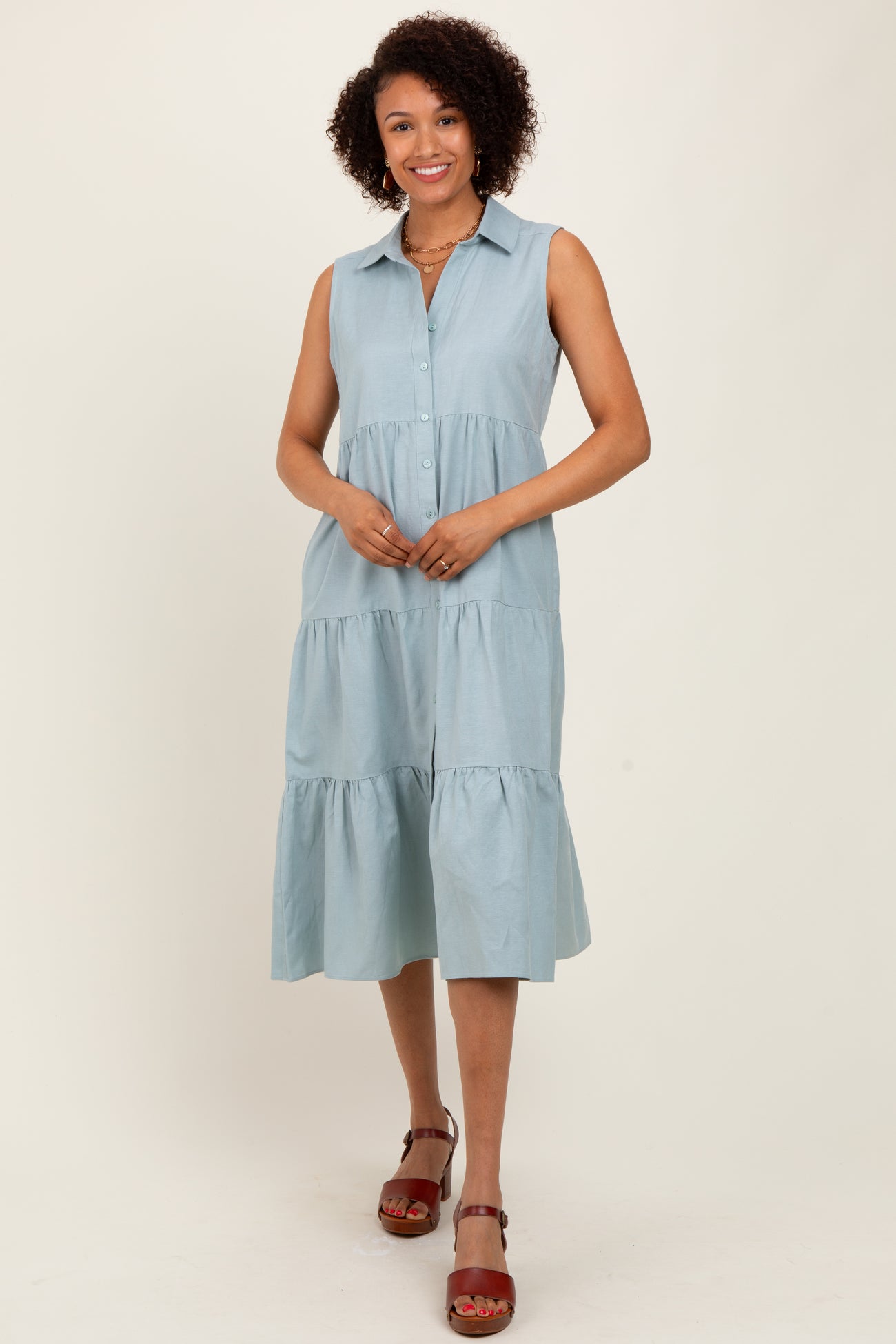 woman wearing a light blue sleeveless button-up tiered dress with a collared neckline and a flowy silhouette