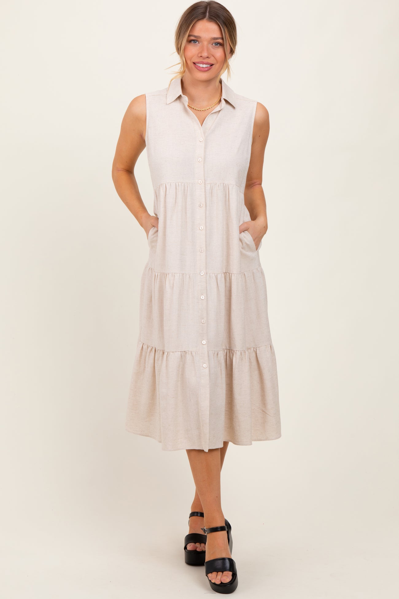woman wearing a beige button-up sleeveless midi dress with pockets and tiered ruffle detailing