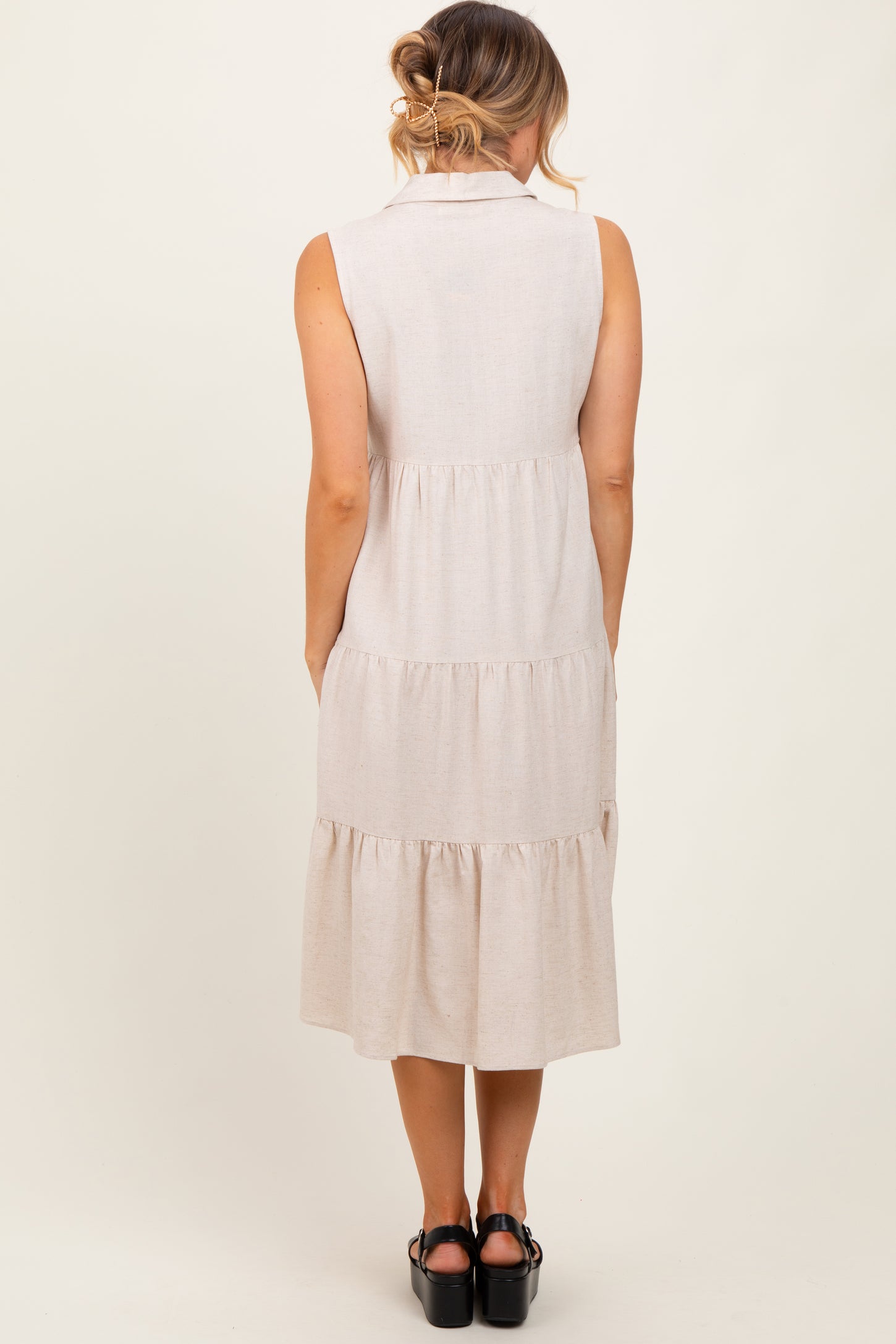 woman wearing a sleeveless beige tiered midi dress with a collared neckline, viewed from the back
