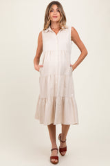 woman wearing a beige sleeveless maternity dress with a button-down front and tiered skirt, holding her baby bump