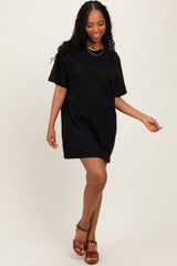 woman wearing a black oversized t-shirt dress and brown heeled sandals, posing with one hand on her hip