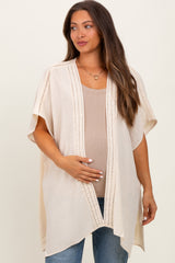 woman wearing a light beige maternity cardigan over a tan tank top and holding her baby bump