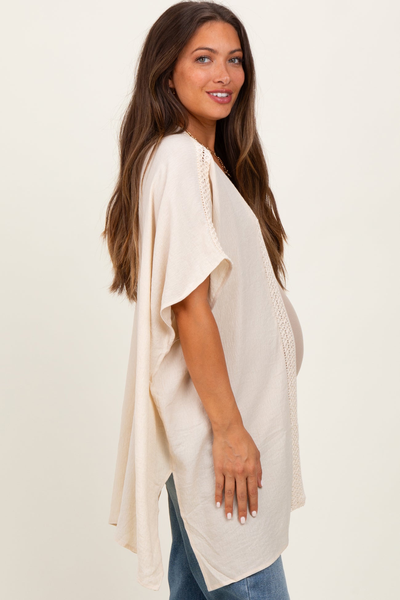woman wearing a cream maternity kimono with crochet trim and a visible baby bump, styled with blue jeans