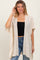 woman wearing a beige loose-fitting cardigan with lace details over a black crop top and blue jeans