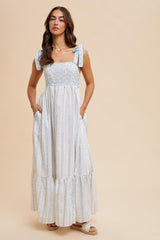 woman wearing a white and light blue floral maxi dress with adjustable tie straps and side pockets
