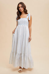 woman wearing a white and light blue floral maxi dress with tie straps and a ruffled hem