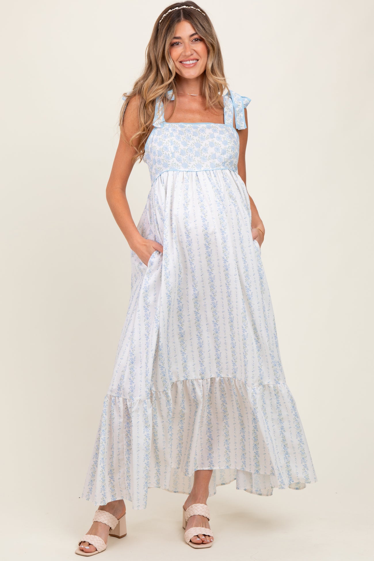 woman wearing a blue and white floral maternity maxi dress with tie straps and pockets, featuring a baby bump