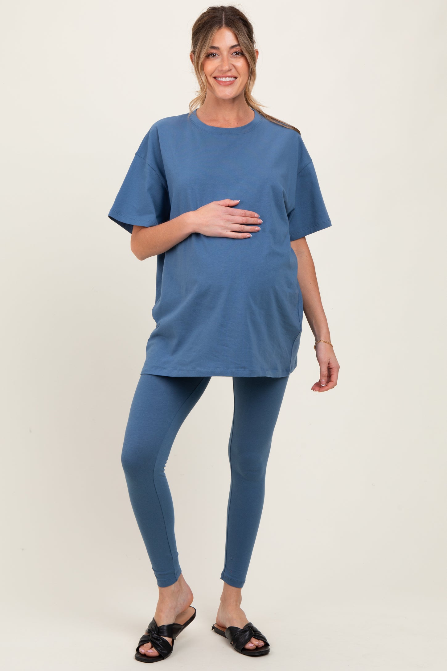 woman wearing a blue maternity t-shirt and matching leggings, gently holding her baby bump