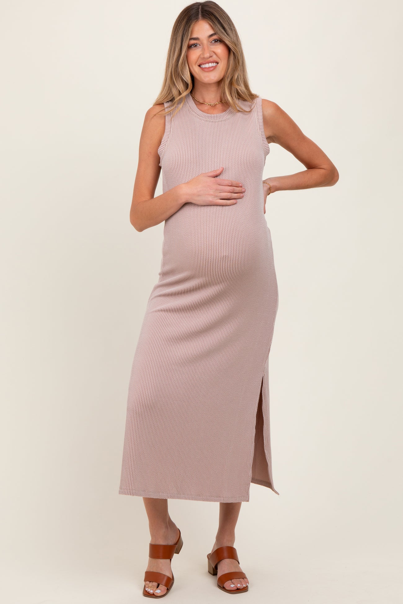 woman wearing a blush ribbed maternity dress with a side slit and holding her baby bump