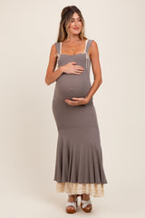 woman wearing a gray maternity dress with tie straps, fitted bodice, and flared skirt, holding her baby bump
