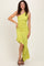 woman wearing a one-shoulder lime green ruched dress with a flounced hem and high slit, standing and smiling