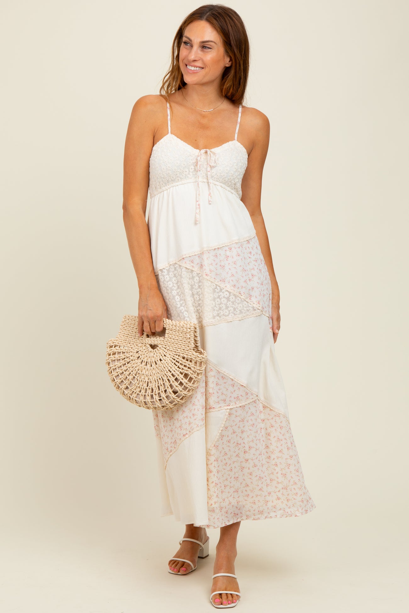 woman wearing a white and floral maxi dress with spaghetti straps, holding a woven bag