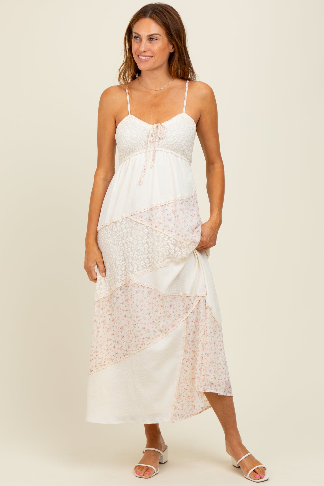woman wearing a white maxi dress with floral print and lace details, standing and smiling