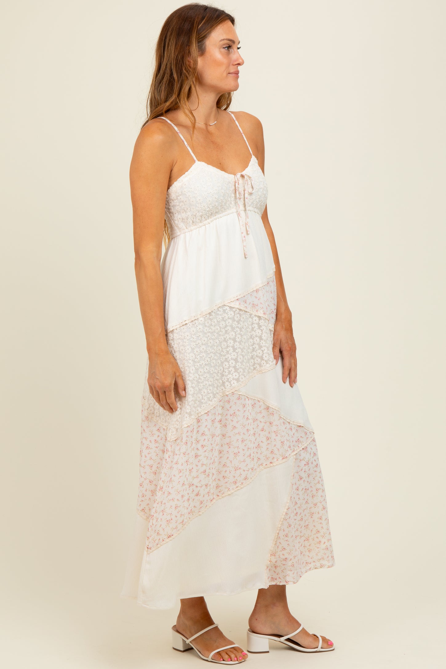 woman wearing a white floral maxi dress with spaghetti straps and tiered patterns, standing in profile