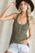 woman wearing a green ribbed tank top with button details and distressed denim shorts, accessorized with a wide-brim hat