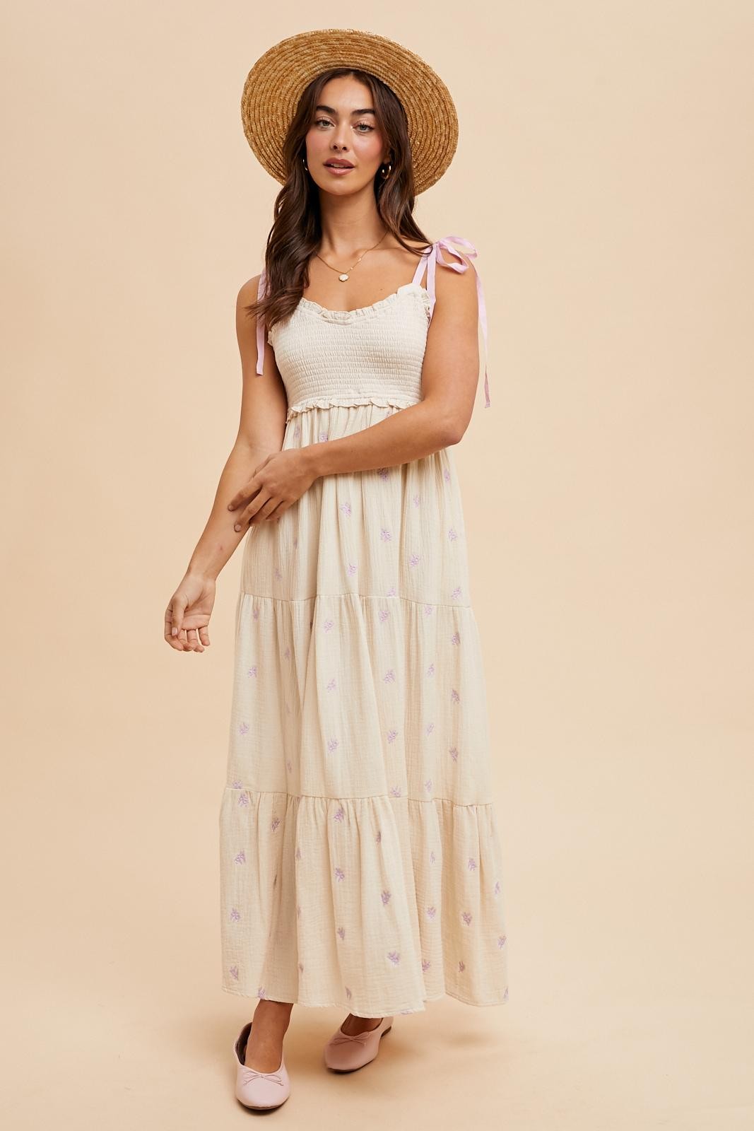 woman wearing a floral patterned cream maxi dress with a smocked bodice and tie straps, paired with a straw hat