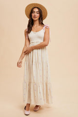 woman wearing a floral patterned cream maxi dress with a smocked bodice and tie straps, paired with a straw hat