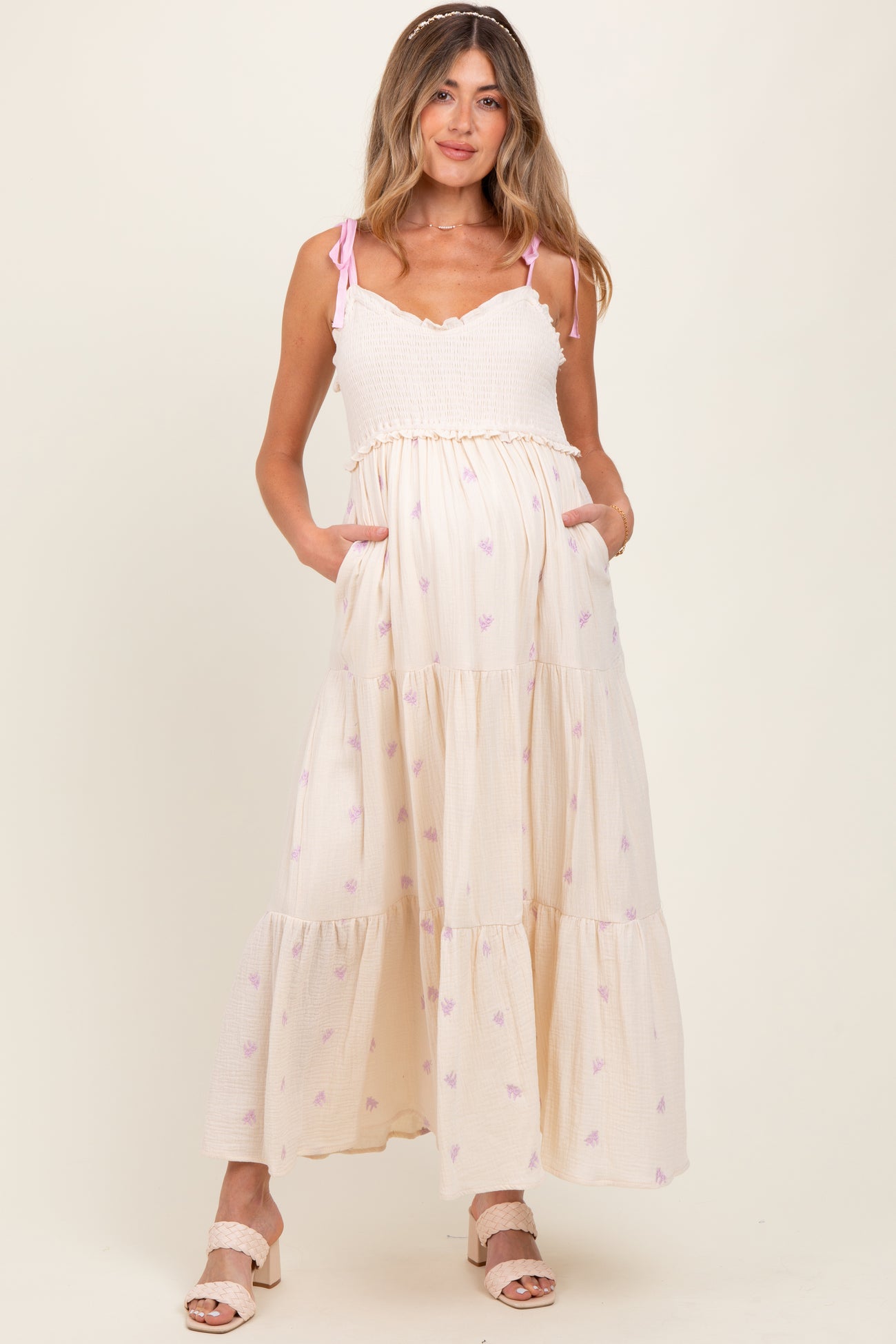 woman wearing a cream maternity maxi dress with pink floral patterns and pockets, showing her baby bump