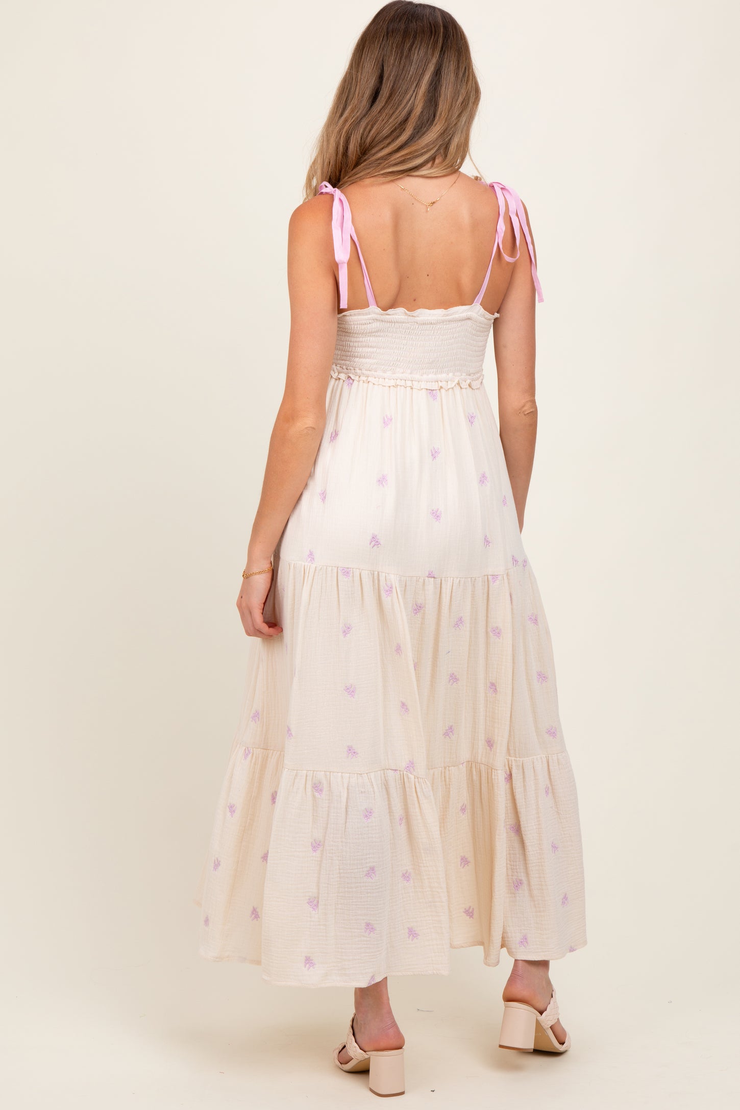 woman wearing a cream maternity maxi dress with purple floral patterns and adjustable spaghetti straps, showing a baby bump