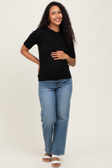 woman wearing a black short sleeve ribbed maternity top and light blue jeans, holding her baby bump