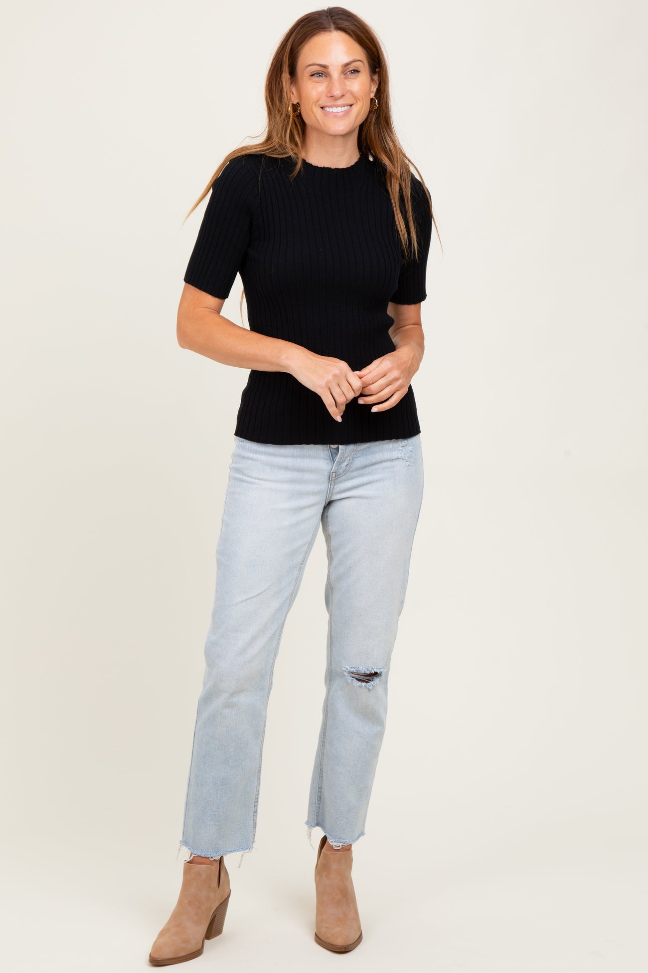 woman wearing a black ribbed short sleeve top and light blue distressed jeans with beige ankle boots