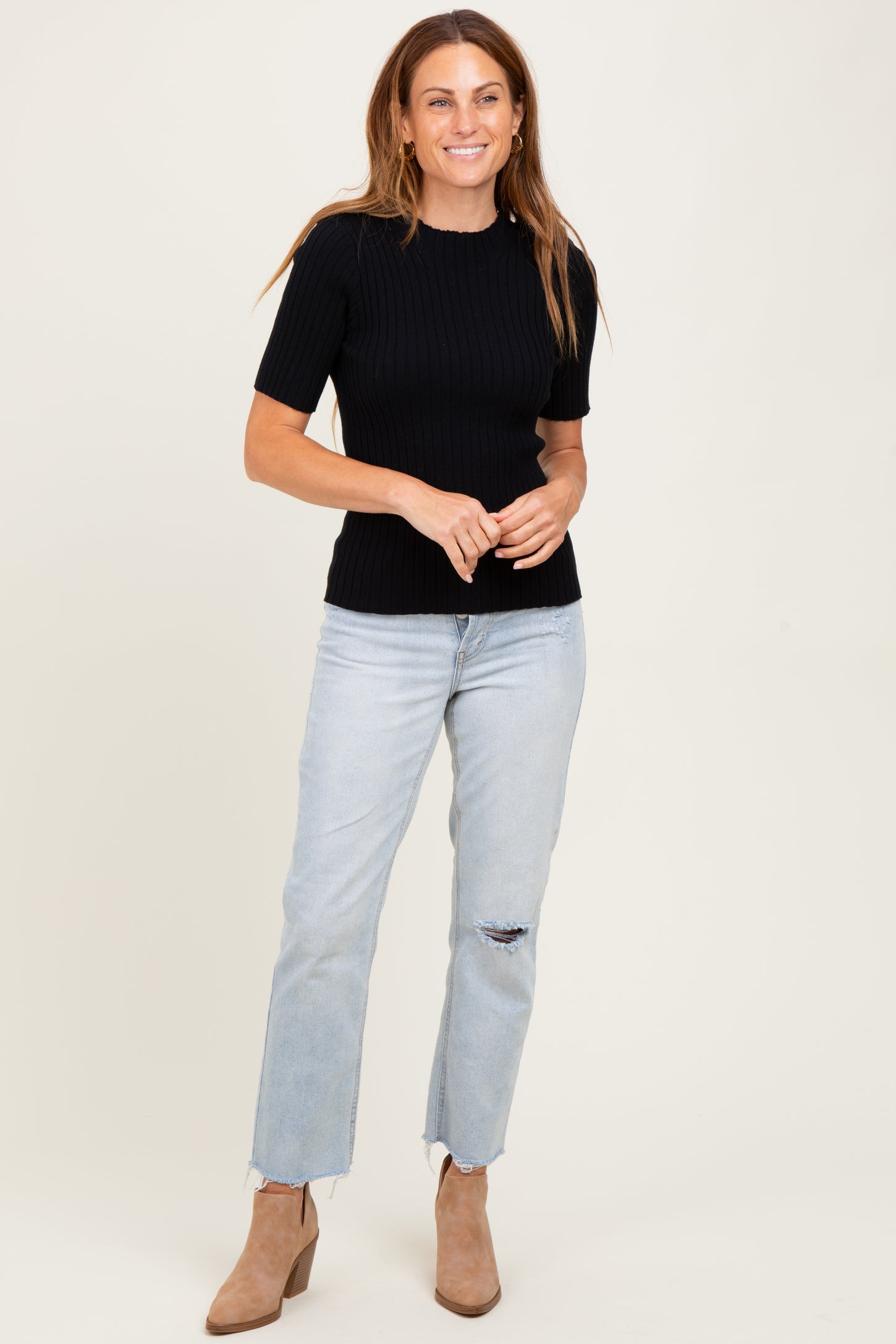 woman wearing a black ribbed short sleeve top and light blue distressed jeans with beige ankle boots