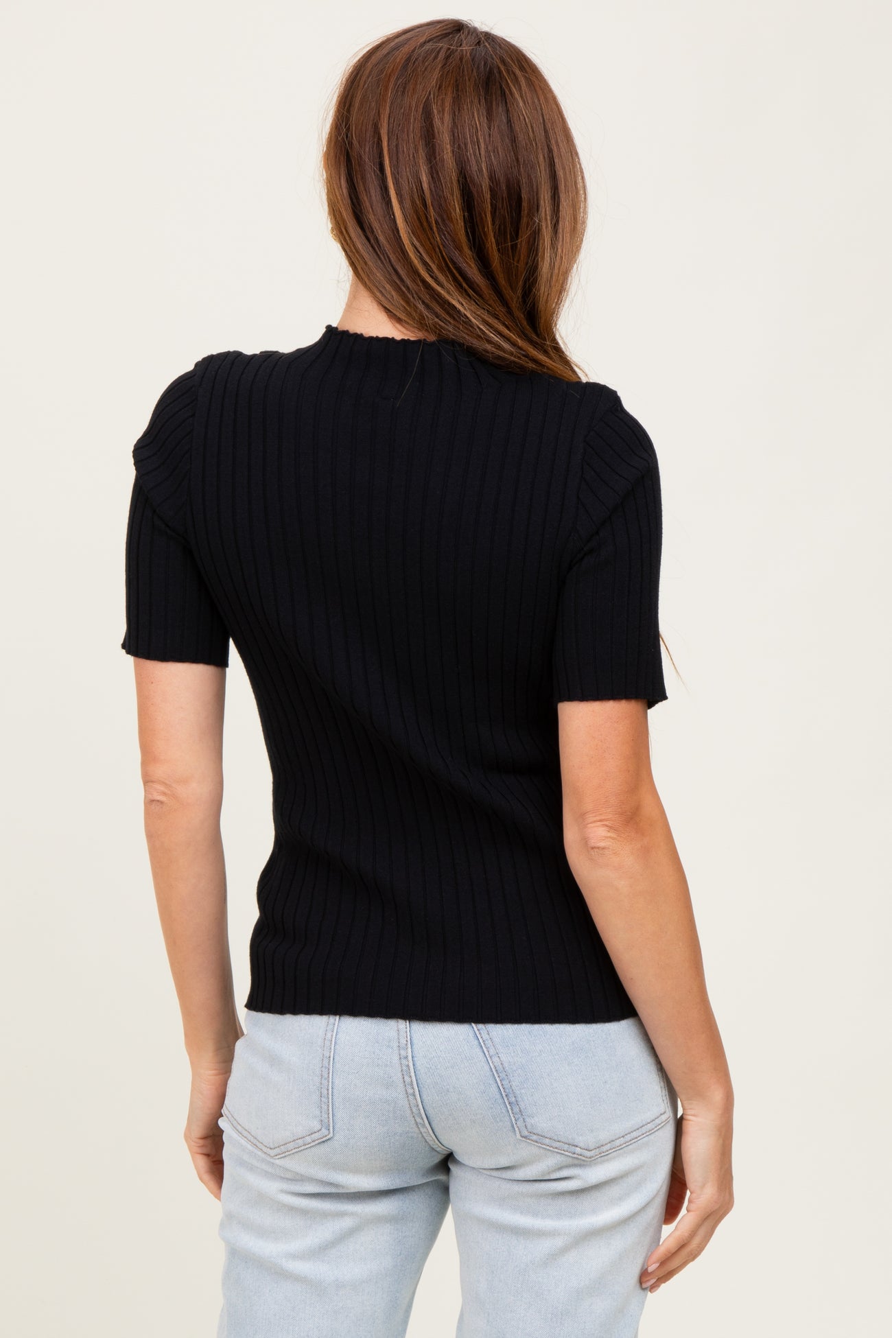 woman wearing a black ribbed short sleeve top with a fitted silhouette and round neckline, viewed from the back