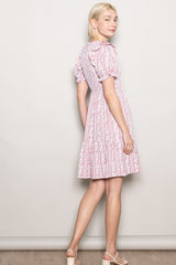 woman wearing a pink floral print puff sleeve dress with a tiered skirt, standing sideways against a neutral backdrop