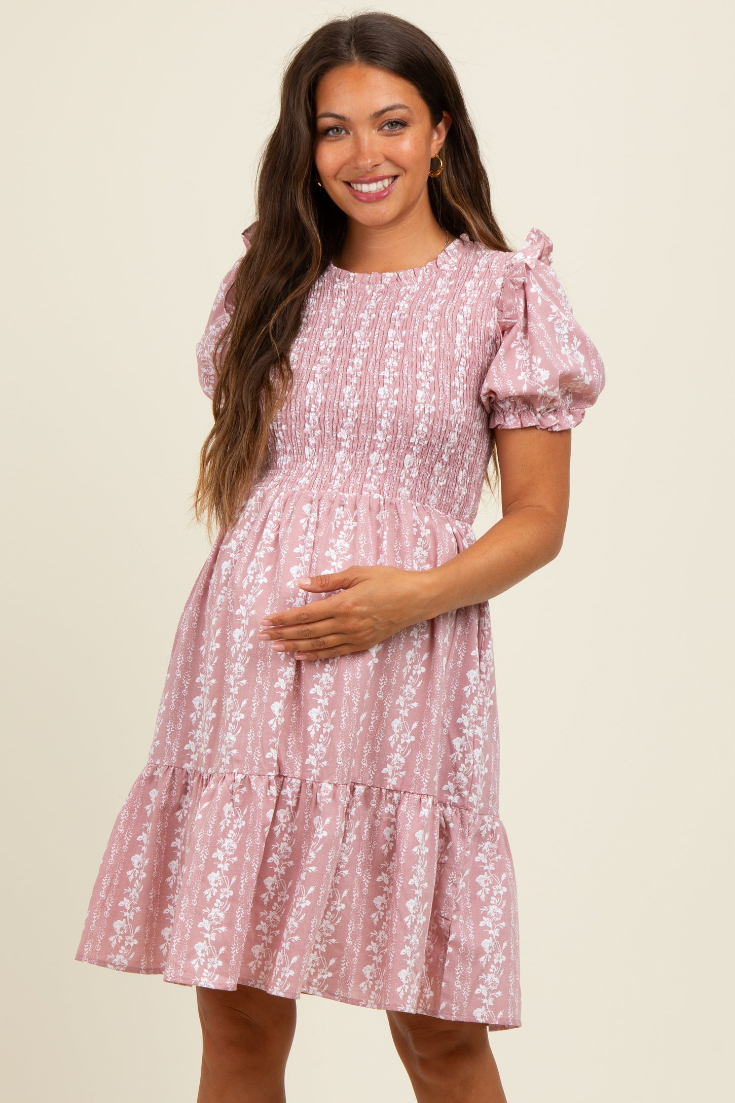 woman wearing a light pink floral maternity dress with puff sleeves and a tiered skirt, showcasing her baby bump