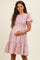 woman wearing a light pink floral maternity dress with puff sleeves and a tiered skirt, showcasing her baby bump