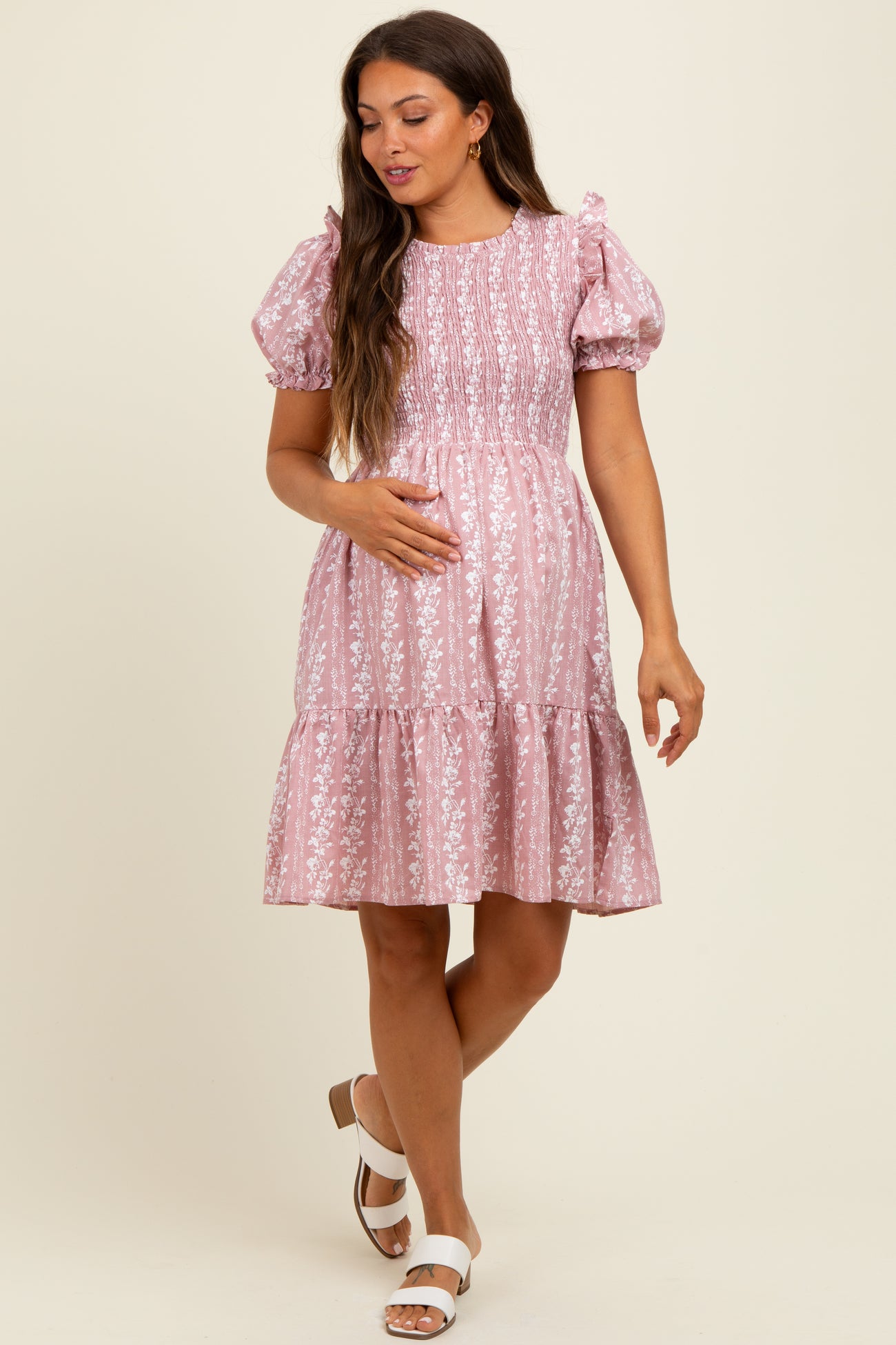 woman wearing a pink floral print smocked maternity dress with puff sleeves and a tiered skirt, holding her baby bump