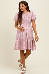 woman wearing a pink floral print smocked maternity dress with puff sleeves and a tiered skirt, holding her baby bump