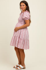 woman wearing a light pink floral maternity dress with puff sleeves and a tiered skirt, showing her baby bump