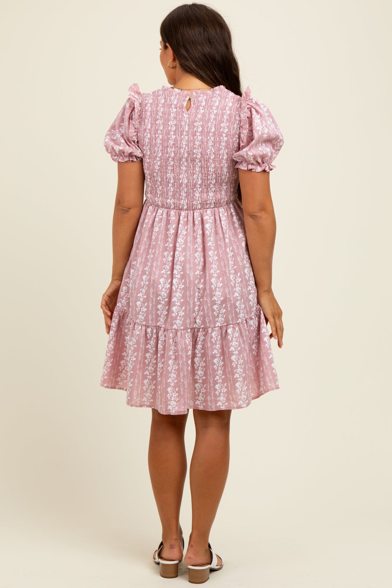 woman wearing a pink floral print maternity dress with puff sleeves and a tiered skirt, seen from the back