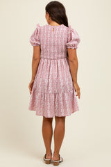 woman wearing a pink floral print maternity dress with puff sleeves and a tiered skirt, seen from the back
